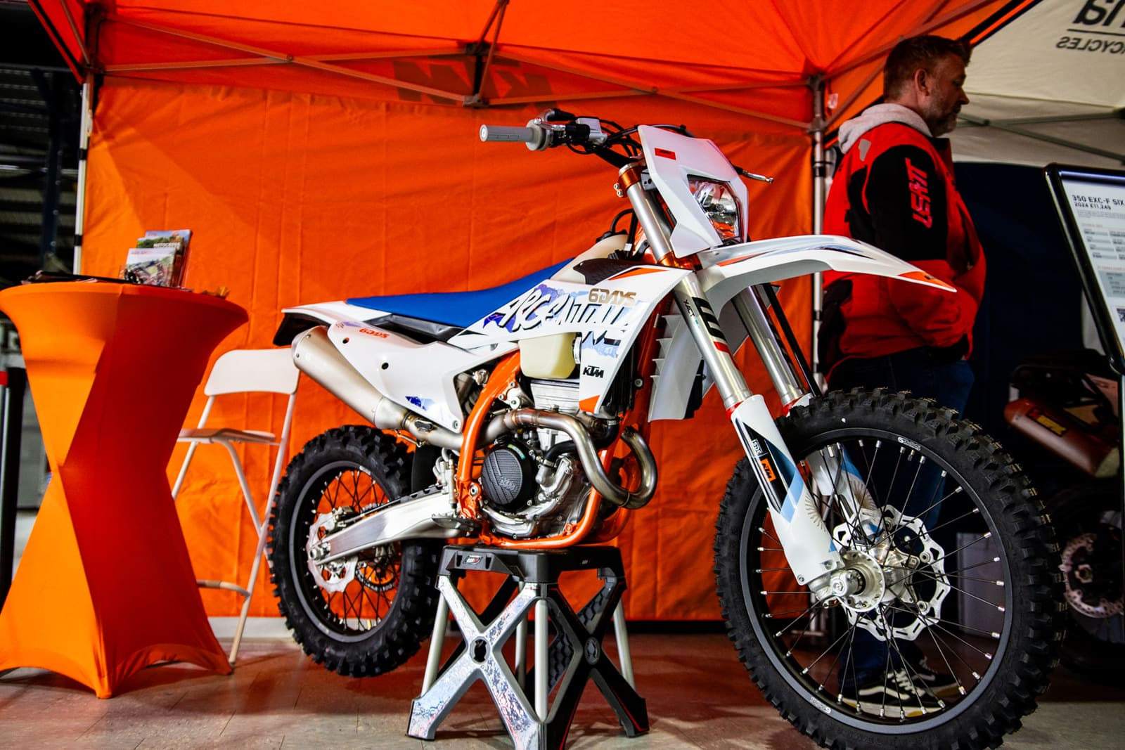 KTM enduro bike on a paddock stand under the race tent, front forks in view.